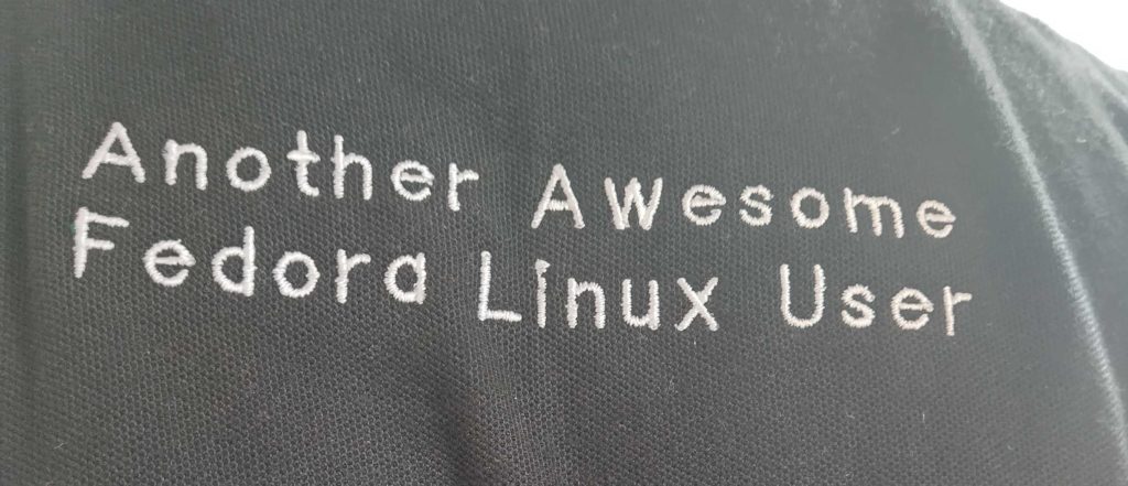 Back of person wearing a polo shirt with the text, Another Awesome Fedora Linux User, embroidered on the shirt